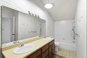 Bathroom featuring double vanity, lofted ceiling, shower / bath combination, and light flooring