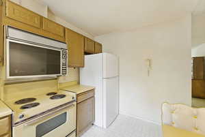 Kitchen featuring light countertops, white appliances, wood finish cabinets, and lofted ceiling