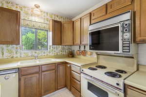 Kitchen featuring white appliances, wood finish cabinetry, light countertops, and wallpapered walls