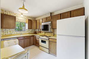 Kitchen with white appliances, light countertops, pendant lighting, wood finish cabinetry, and wallpapered walls
