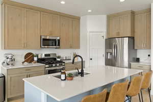 Kitchen with stainless steel appliances, a center island with sink, light stone counters, light wood finish cabinets, and recessed lighting