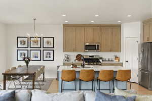 Kitchen featuring stainless steel appliances, light wood-style floors, an island with sink, and a breakfast bar