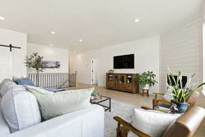 Living room with a barn door, light wood-style floors, and recessed lighting