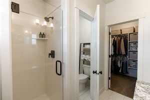 Bathroom with a shower stall, a spacious closet, and light colored carpet