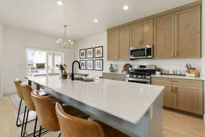 Kitchen with light wood finished floors, stainless steel appliances, a kitchen island with sink, and a breakfast bar