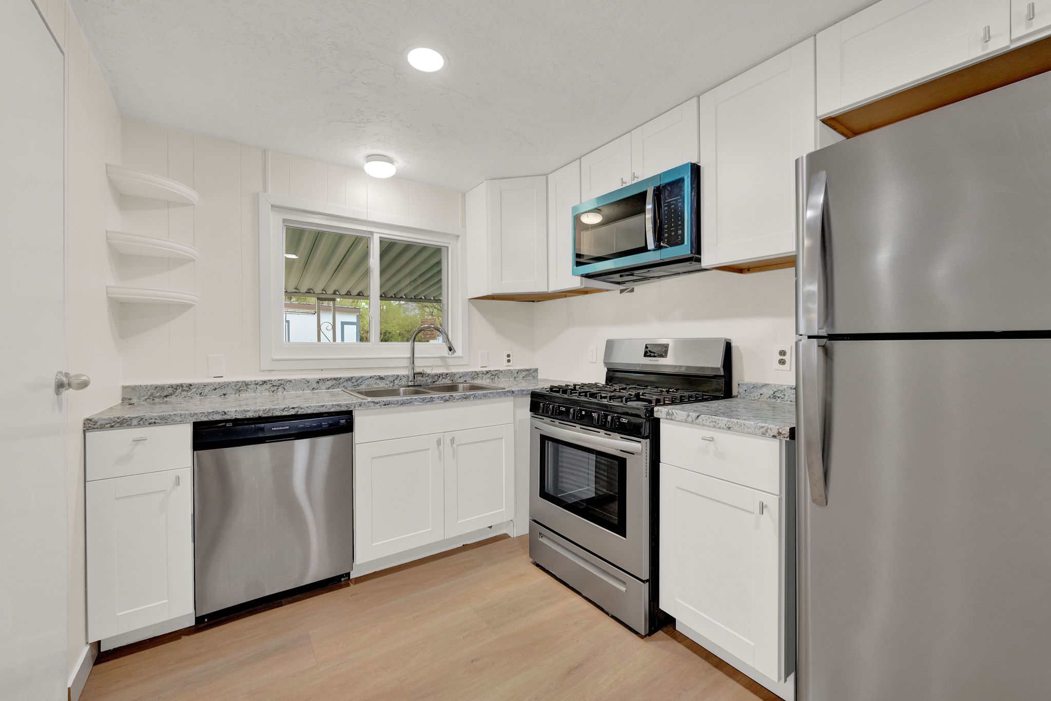 Kitchen featuring stainless steel appliances, white cabinetry, open shelves, light wood-type flooring, and light stone counters