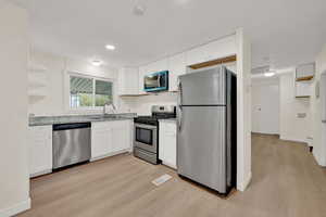 Kitchen featuring stainless steel appliances, white cabinets, light wood-style flooring, open shelves, and light stone countertops