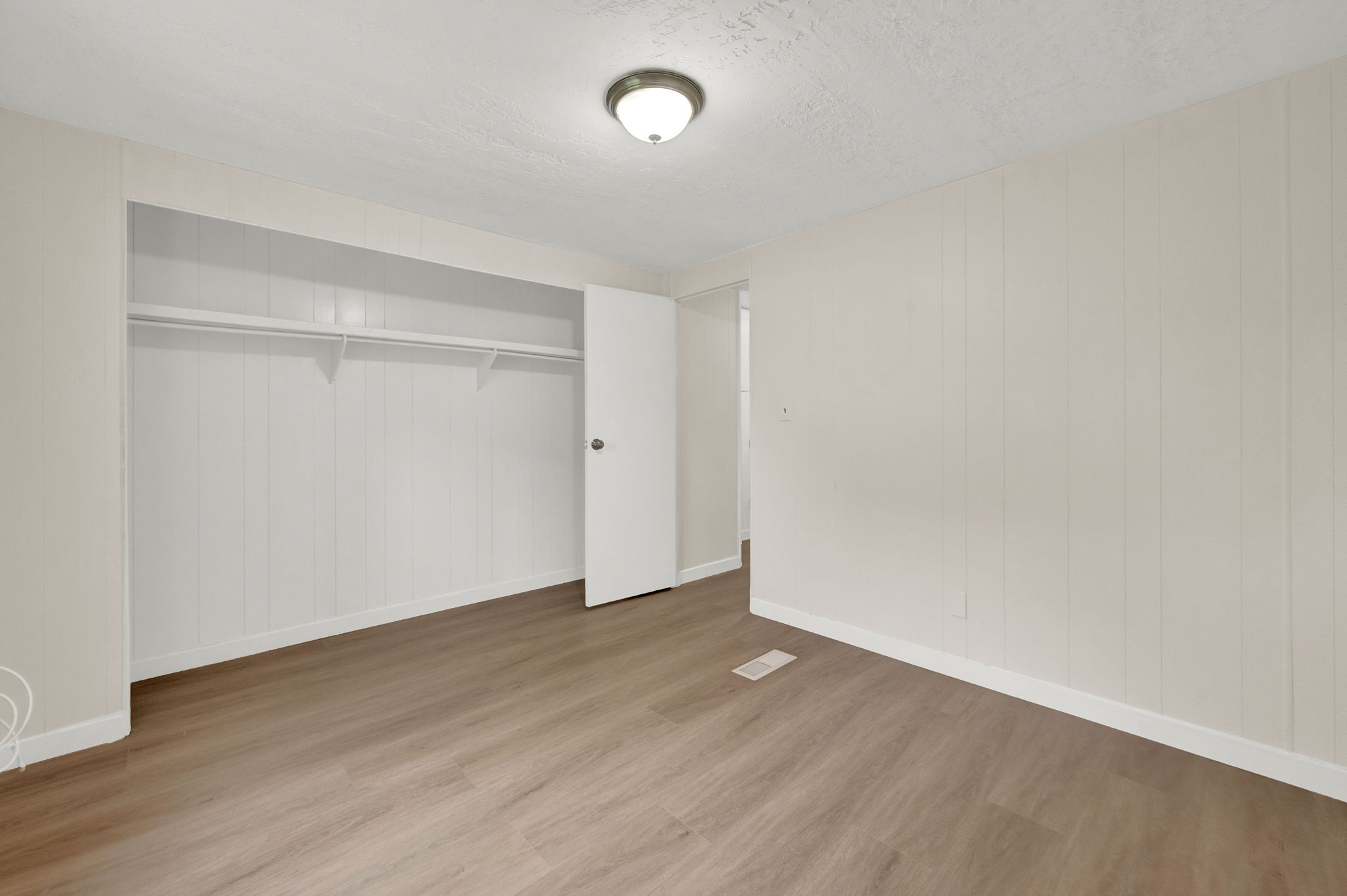 Unfurnished bedroom featuring light wood-style flooring, a closet, a textured ceiling, and wood walls