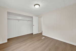 Unfurnished bedroom featuring light wood-style flooring, a closet, a textured ceiling, and wood walls