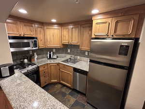Kitchen featuring stainless steel appliances, dark stone finish floors, recessed lighting, light stone counters, and decorative backsplash