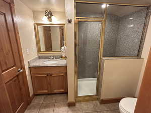 Bathroom with a textured wall, a shower stall, vanity, and light tile patterned floors