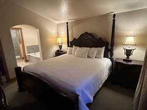 Bedroom with a textured wall, arched walkways, a textured ceiling, and connected bathroom