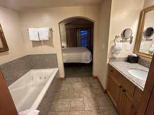 Ensuite bathroom with vanity, a tub with jets, light tile patterned floors, and a textured wall