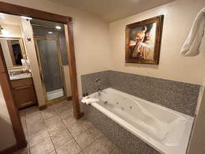 Full bath featuring vanity, a stall shower, a whirlpool tub, a textured wall, and light tile patterned floors