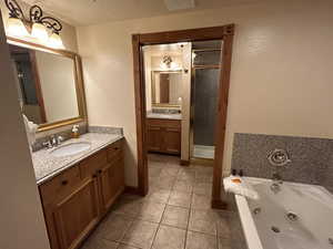 Bathroom featuring a textured wall, two vanities, a shower stall, light tile patterned floors, and a jetted tub