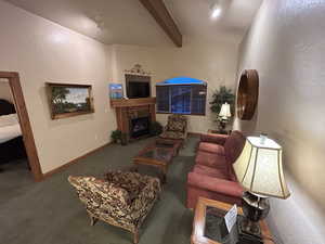 Carpeted living room featuring a fireplace with flush hearth, lofted ceiling with beams.