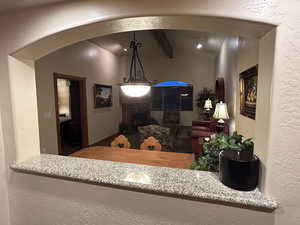 Kitchen featuring a textured wall, vaulted ceiling with beams, and hanging light fixtures