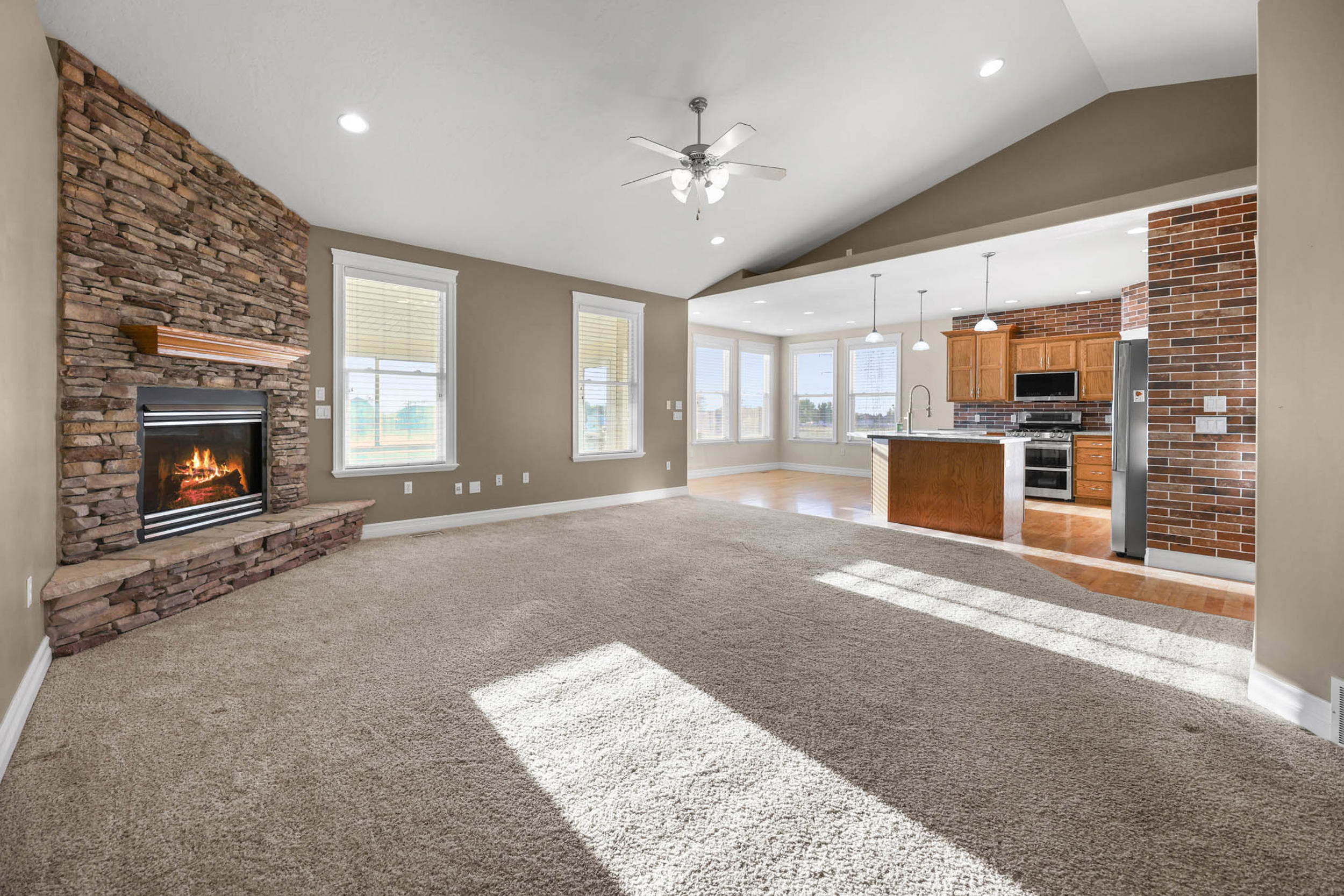 Living room featuring a stone fireplace, light colored carpet, recessed lighting, a ceiling fan, and lofted ceiling. unfurnished