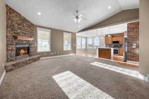 Living room featuring a stone fireplace, light colored carpet, recessed lighting, a ceiling fan, and lofted ceiling. unfurnished