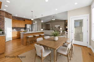 Open-concept kitchen and dining area featuring wood-finish flooring, brick accent wall, recessed lighting, and a kitchen island with pendant lighting. virtually staged