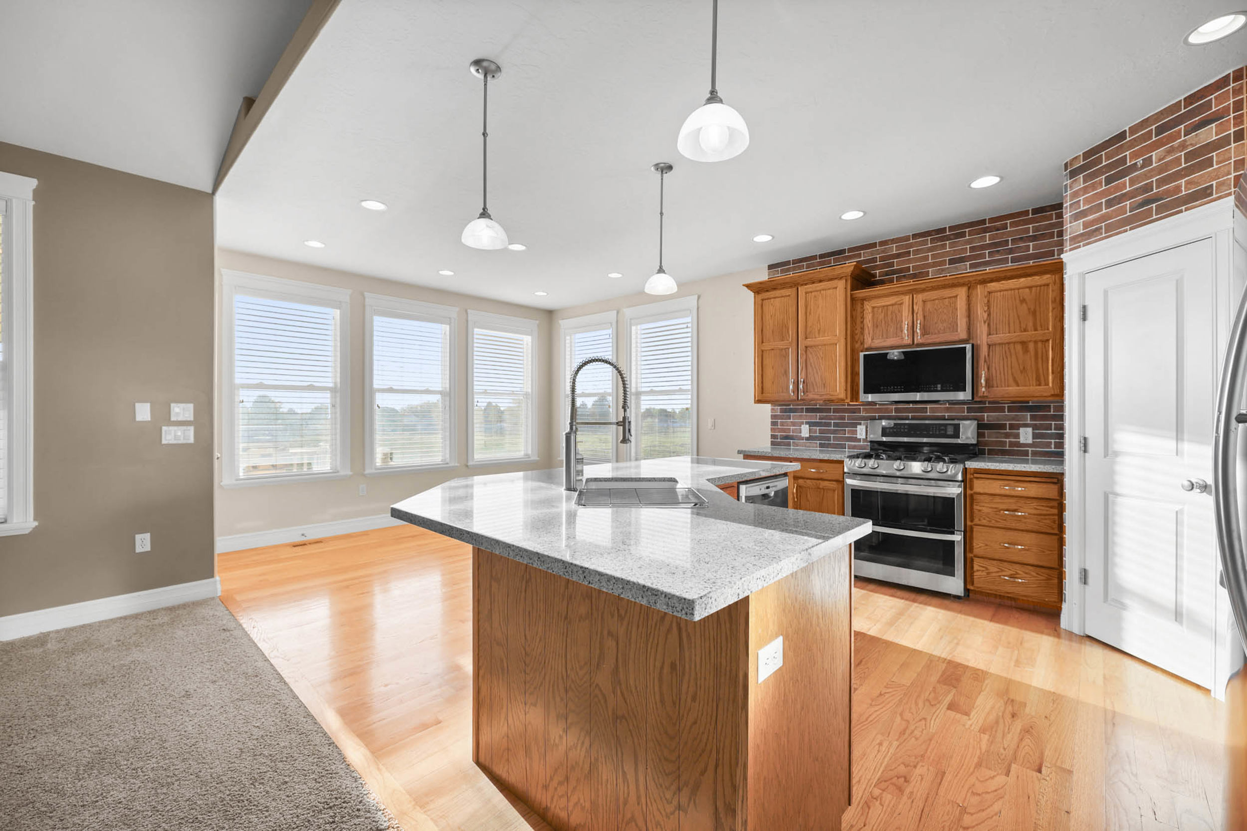 Kitchen featuring wood finish cabinets, stainless steel appliances, an island with sink, light stone countertops, and pendant lighting