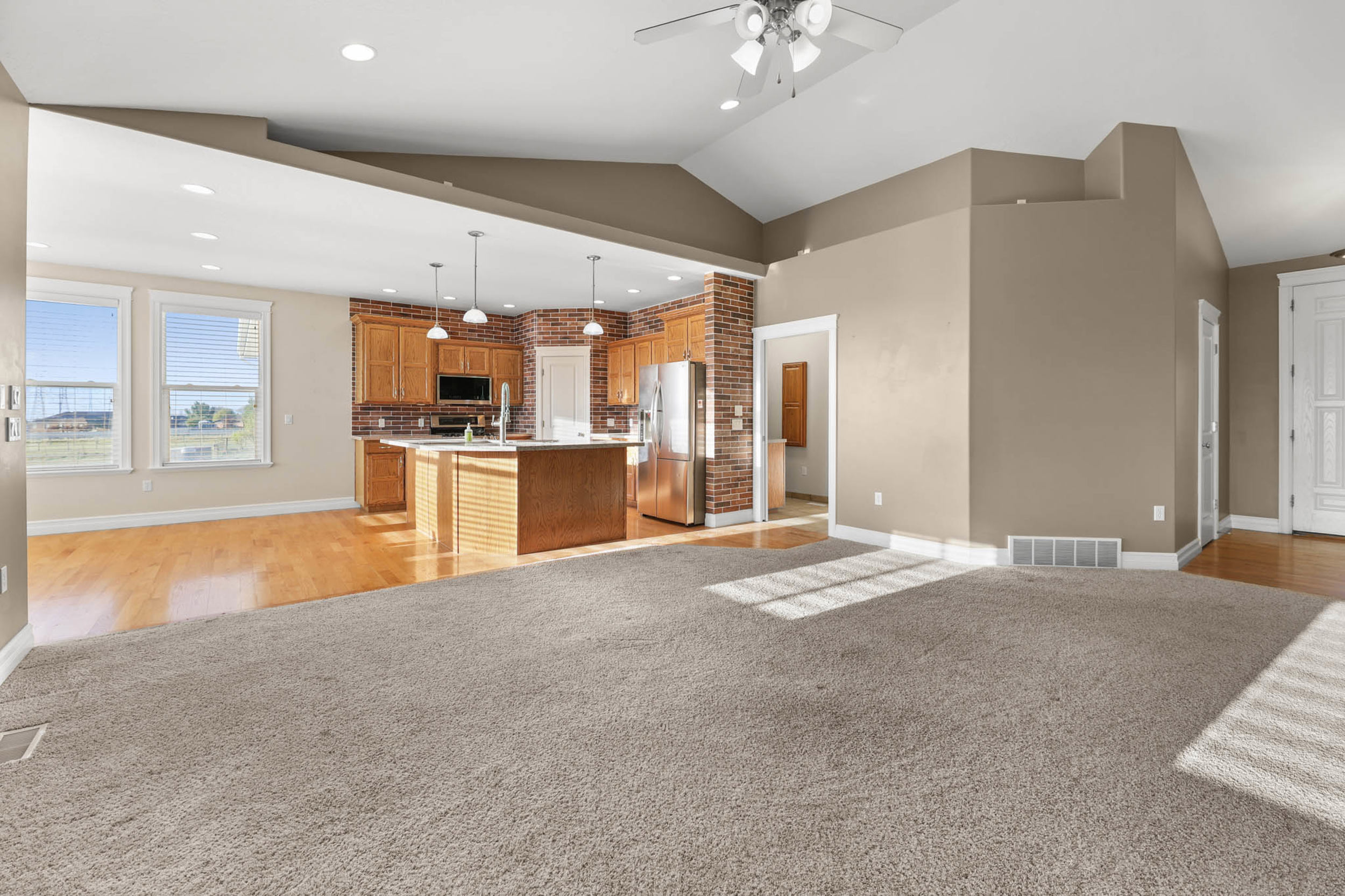 Kitchen featuring open floor plan, a center island with sink, light colored carpet, wood finish cabinetry, and stainless steel appliances. unfurnished