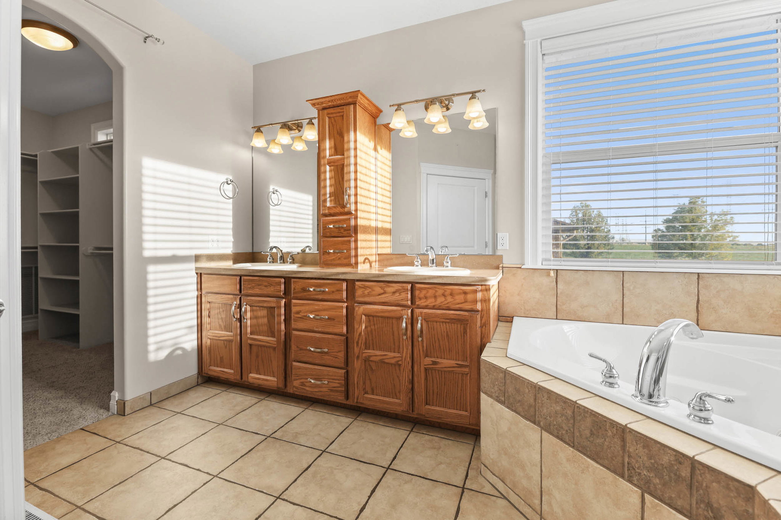 Dual vanity primary ensuite bath  with wood cabinetry and countertop, featuring dual sinks and an integrated tall storage cabinet