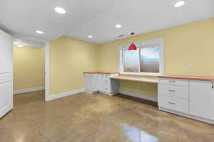 Bedroom/craft room/office with built in study area, white cabinetry, concrete flooring, and wooden counters. Huge closet