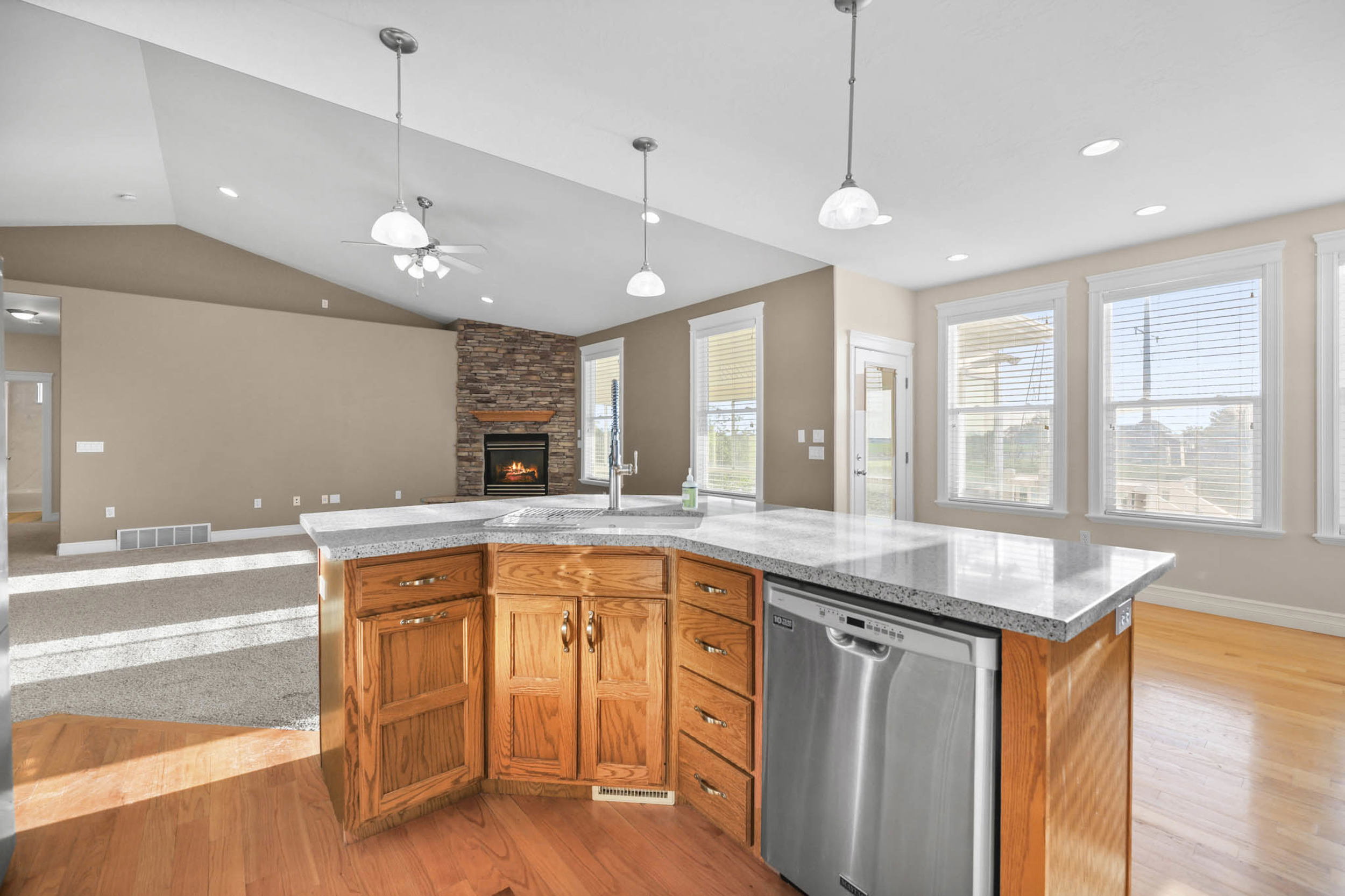 Kitchen featuring a kitchen island with sink, a fireplace, stainless steel dishwasher, light wood-style floors, and wood finish cabinetry