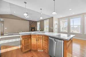 Kitchen featuring a kitchen island with sink, a fireplace, stainless steel dishwasher, light wood-style floors, and wood finish cabinetry