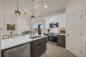 Kitchen with stainless steel appliances, dual tone cabinets, decorative light fixtures, light stone countertops, and tasteful backsplash