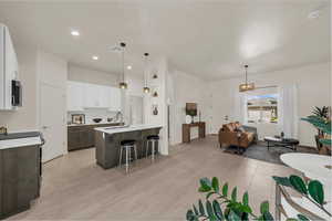 Kitchen featuring two tone cabinetry, a breakfast bar area, open floor plan, pendant lighting, and light stone countertops