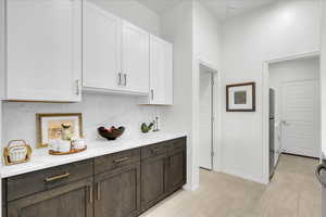 Bar area with dual tone cabinetry, decorative backsplash, light stone countertops, and fridge