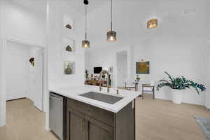 Kitchen with decorative light fixtures, light stone counters, dark wood finish cabinetry, stainless steel dishwasher, and a peninsula