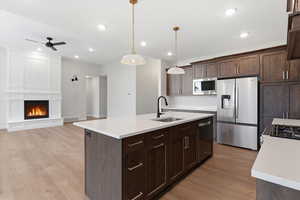 Kitchen featuring stainless steel appliances, a center island with sink, pendant lighting, ceiling fan, and dark wood finish cabinetry