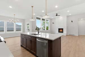 Kitchen featuring dark wood finish cabinetry, light wood-style floors, dishwasher, and an island with sink