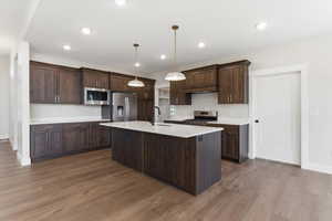 Kitchen with stainless steel appliances, dark wood-style flooring, pendant lighting, an island with sink, and dark wood finish cabinetry