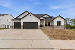 Modern farmhouse with board and batten siding, an attached garage, stone siding, driveway, and roof with shingles