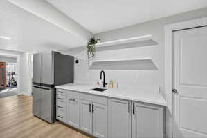 Bar area featuring open shelves, freestanding refrigerator, light wood finished floors, light stone counters, and gray cabinetry