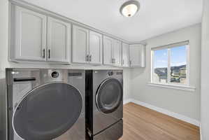 Laundry area with light wood-style flooring, washing machine and dryer, and cabinet space