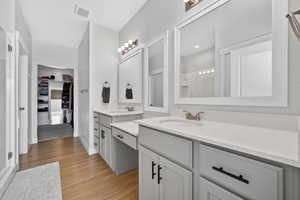 Bathroom featuring two vanities, a stall shower, light wood-type flooring, and a spacious closet