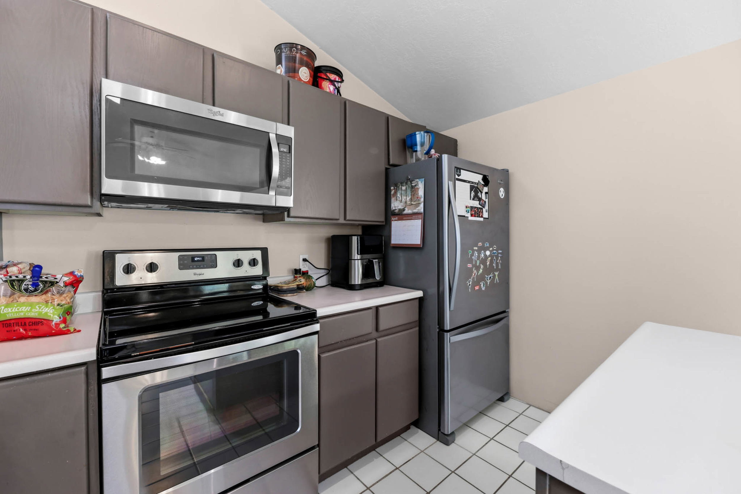 Kitchen with stainless steel appliances, light countertops, vaulted ceiling, light tile patterned floors, and dark wood finish cabinets