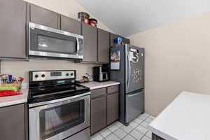 Kitchen with stainless steel appliances, light countertops, vaulted ceiling, light tile patterned floors, and dark wood finish cabinets
