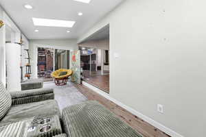 Living area with vaulted ceiling, a skylight, light wood-style floors, and recessed lighting