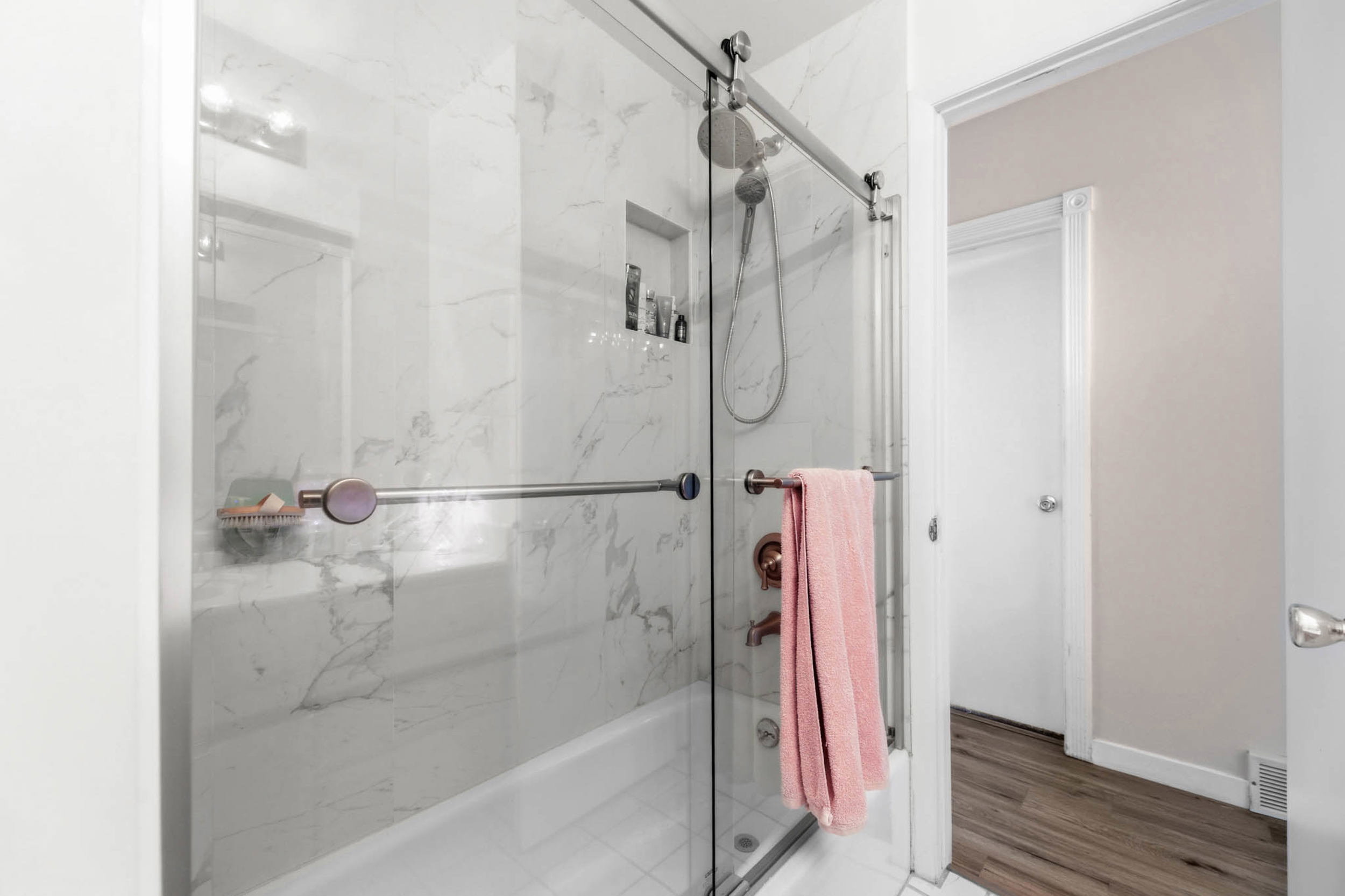 Full bath with enclosed tub / shower combo and light wood finished floors