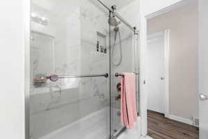 Full bath with enclosed tub / shower combo and light wood finished floors