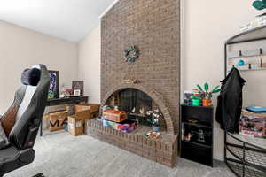 Living area with vaulted ceiling, carpet flooring, a brick fireplace, and a desk