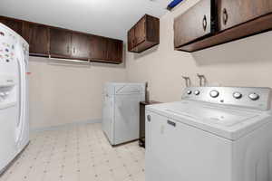 Laundry area featuring light floors, separate washer and dryer, a textured ceiling, and cabinet space