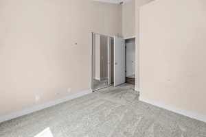Unfurnished bedroom featuring light colored carpet, a high ceiling, and a closet