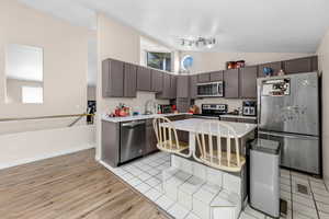 Kitchen featuring lofted ceiling, stainless steel appliances, light countertops, light wood-type flooring, and dark wood finish cabinetry